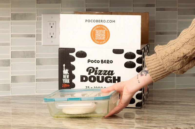 A Poco Bero Pizza Dough box open on a kitchen counter with individually wrapped frozen dough balls beside it